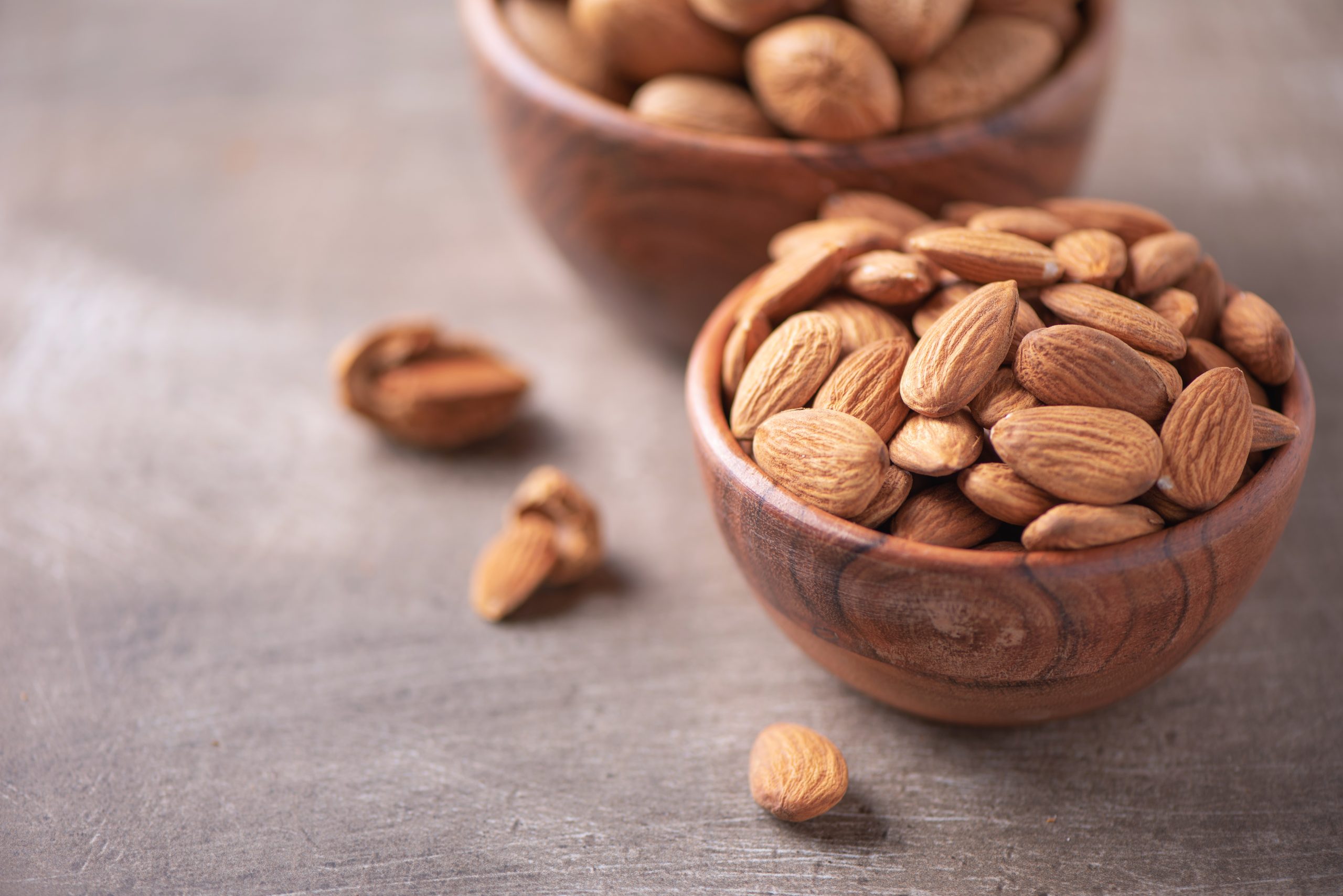 Almond nuts in wooden bowl on wood textured background. Copy space. Superfood, vegan, vegetarian food concept. Macro of almond nut texture, selective focus. Healthy snack