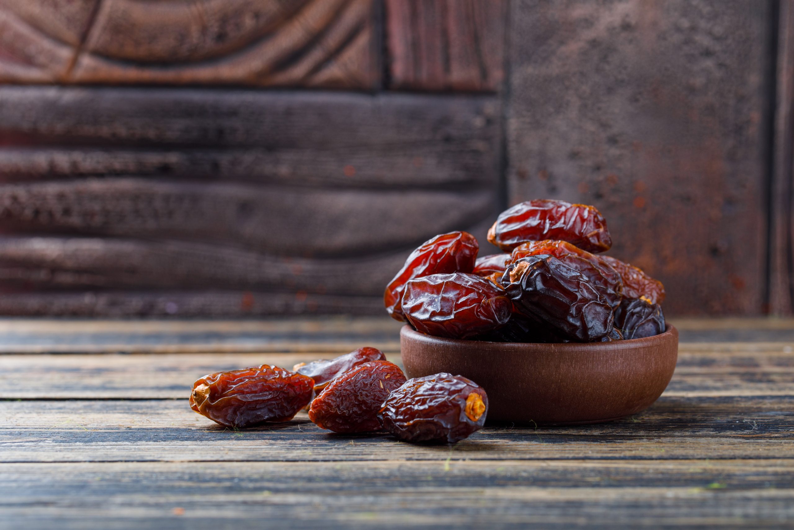 Sweet dates in a clay plate on stone tile and wooden background, side view.